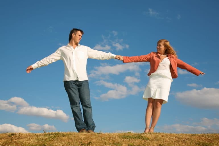 Un hombre sostiene a una mujer, mientras ambos están en un prado bajo el cielo azul.