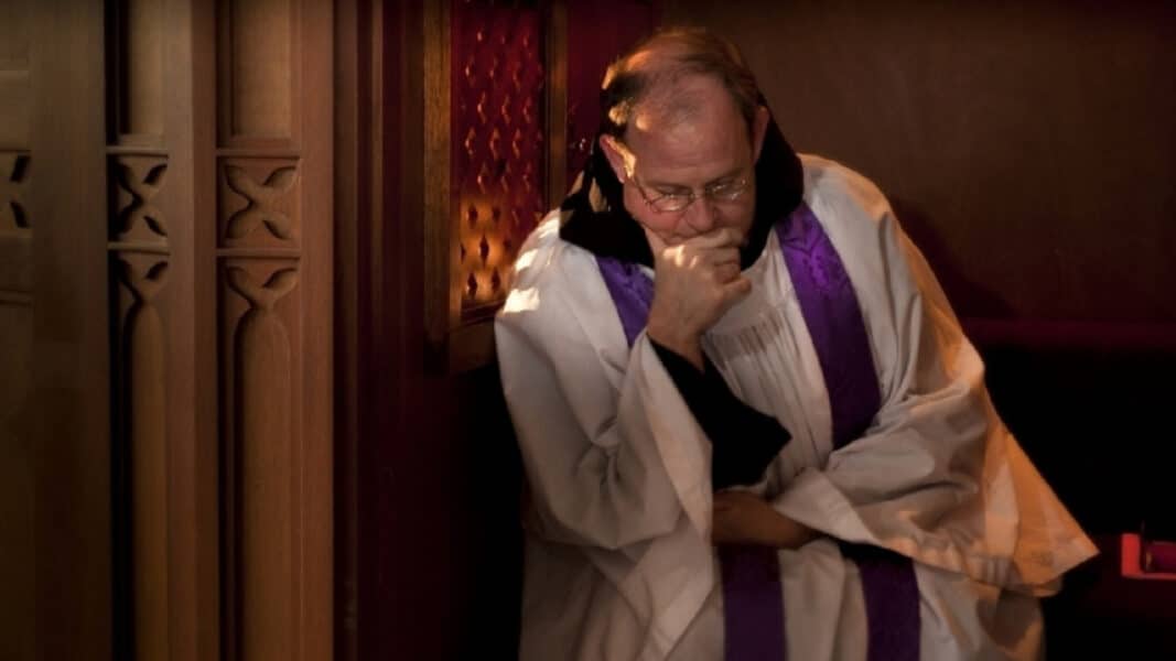 Sacerdote católico pensativo en el confesionario que simboliza el abandono de la confesión católica