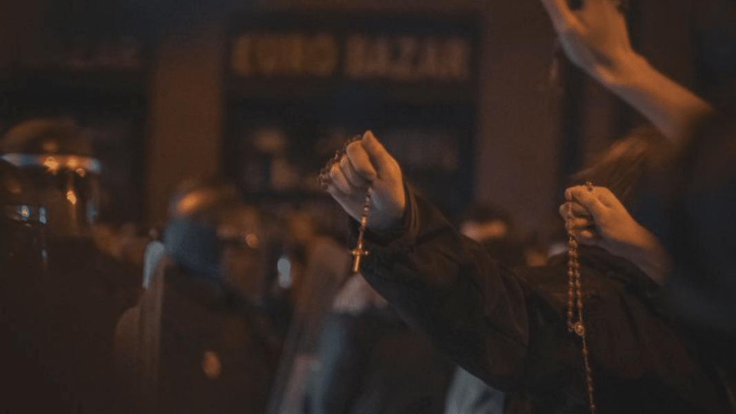 Jóvenes enseñan sus rosarios a los antidisturbios en las protestas en Ferraz