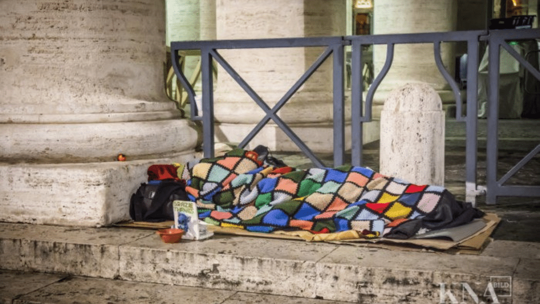 Una imagen que representa que la mayor pobreza es no conocer a Dios, mostrando a una persona sin hogar frente al Vaticano.
