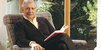 José Luis Olaizola sentado con un libro en las manos, en una sala luminosa