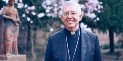 Guy de Kerimel, arzobispo de Toulouse, sonriente en un jardín junto a una estatua religiosa