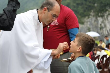 Sacerdote dando la comunión a un niño durante la Jornada Eucarística Mariana Juvenil en Covadonga.