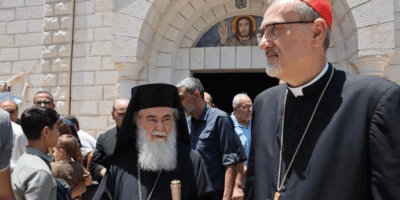 El cardenal Pizzaballa y el Patriarca Teófilo III tras su visita a Gaza, frente a una iglesia rodeados de fieles.
